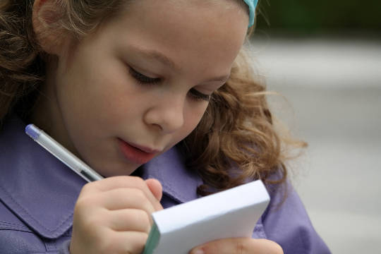 a young girl intently writing on a pad of paper